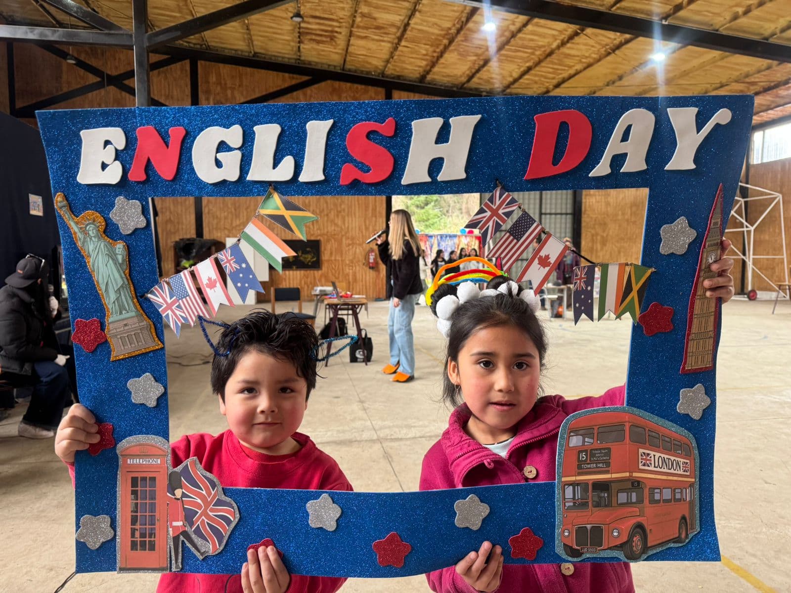 Dos estudiantes con adornos en el cabello junto al marco English Day