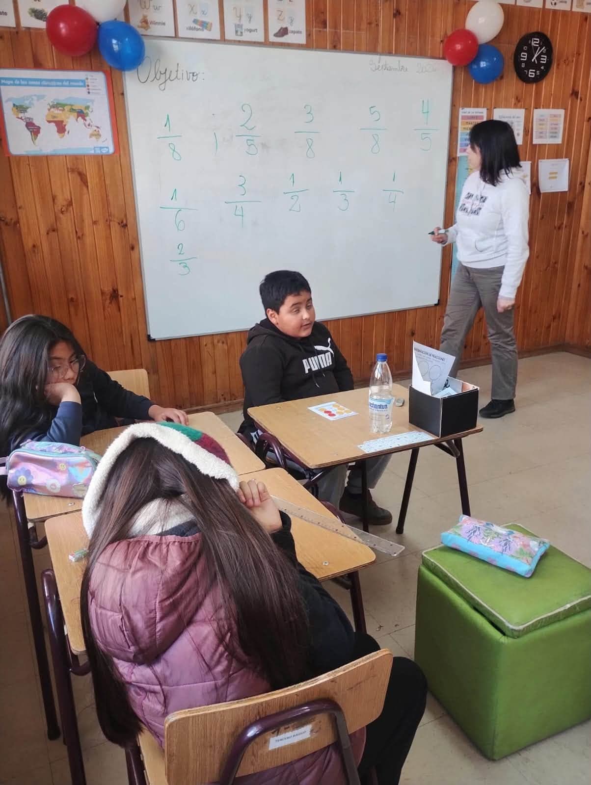 Estudiantes participan en una clase sobre fracciones junto a su profesora