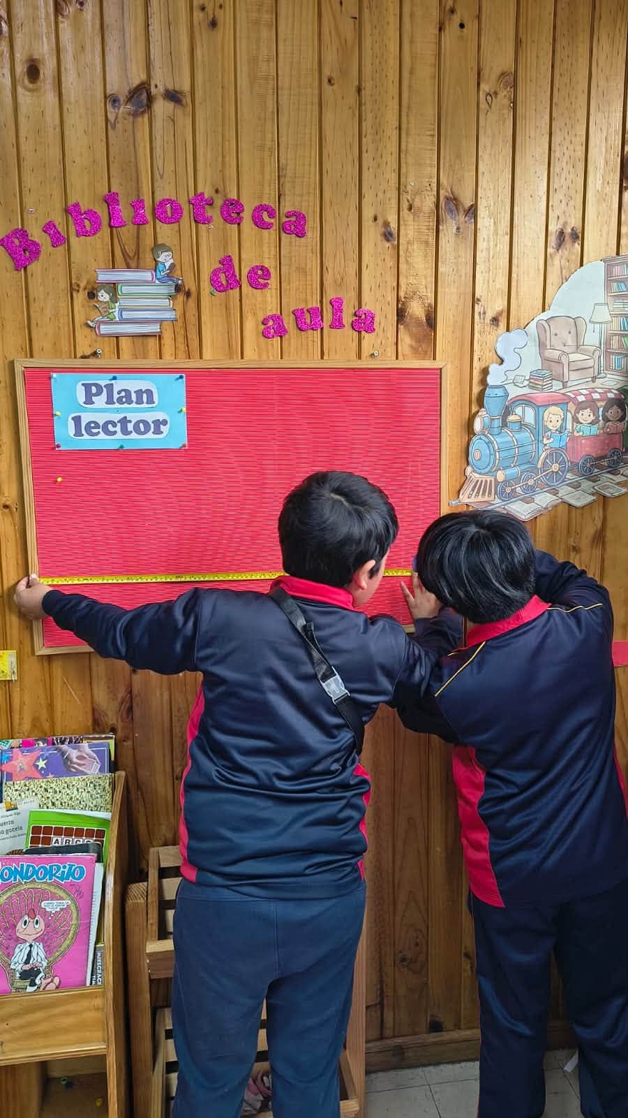 Dos estudiantes utilizan una cinta métrica para medir un panel del aula